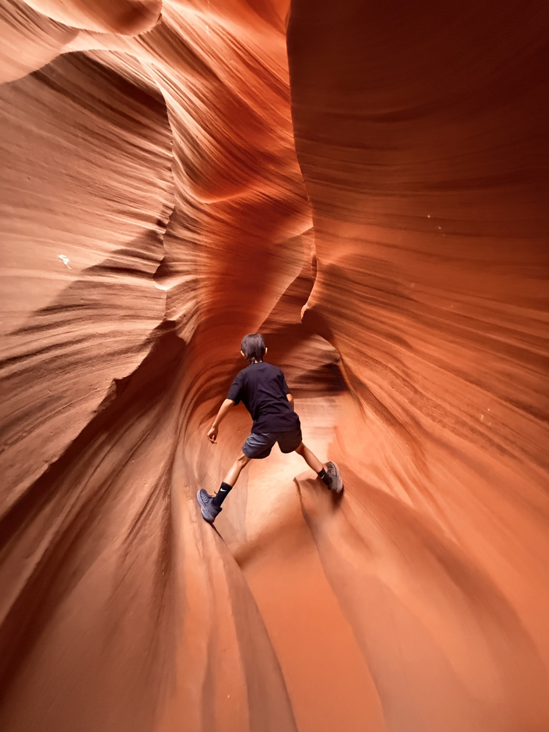 A person is navigating a narrow, winding sandstone canyon with smooth, flowing walls.