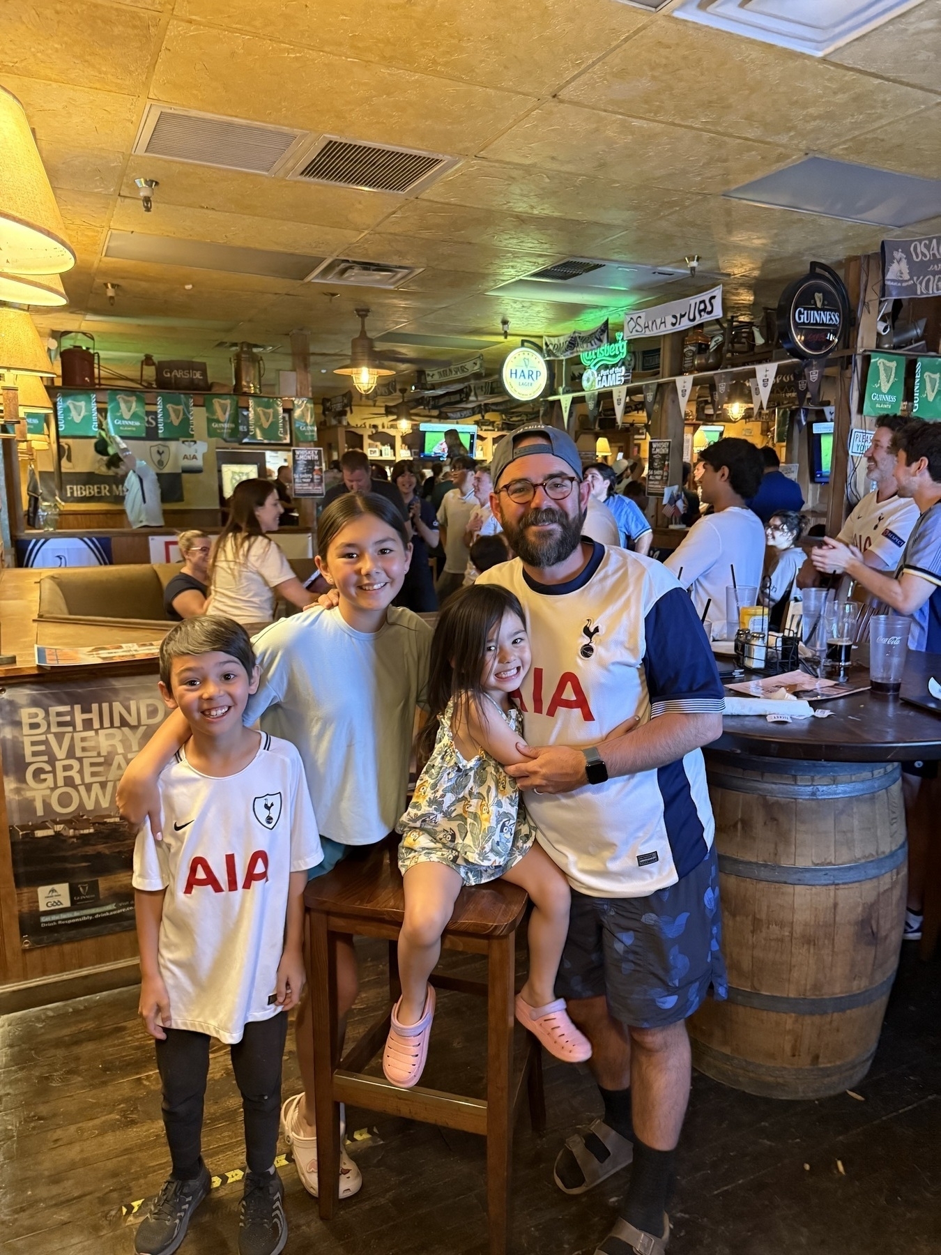 A group of people wearing sports jerseys are gathered in a lively bar with soccer-related decorations.