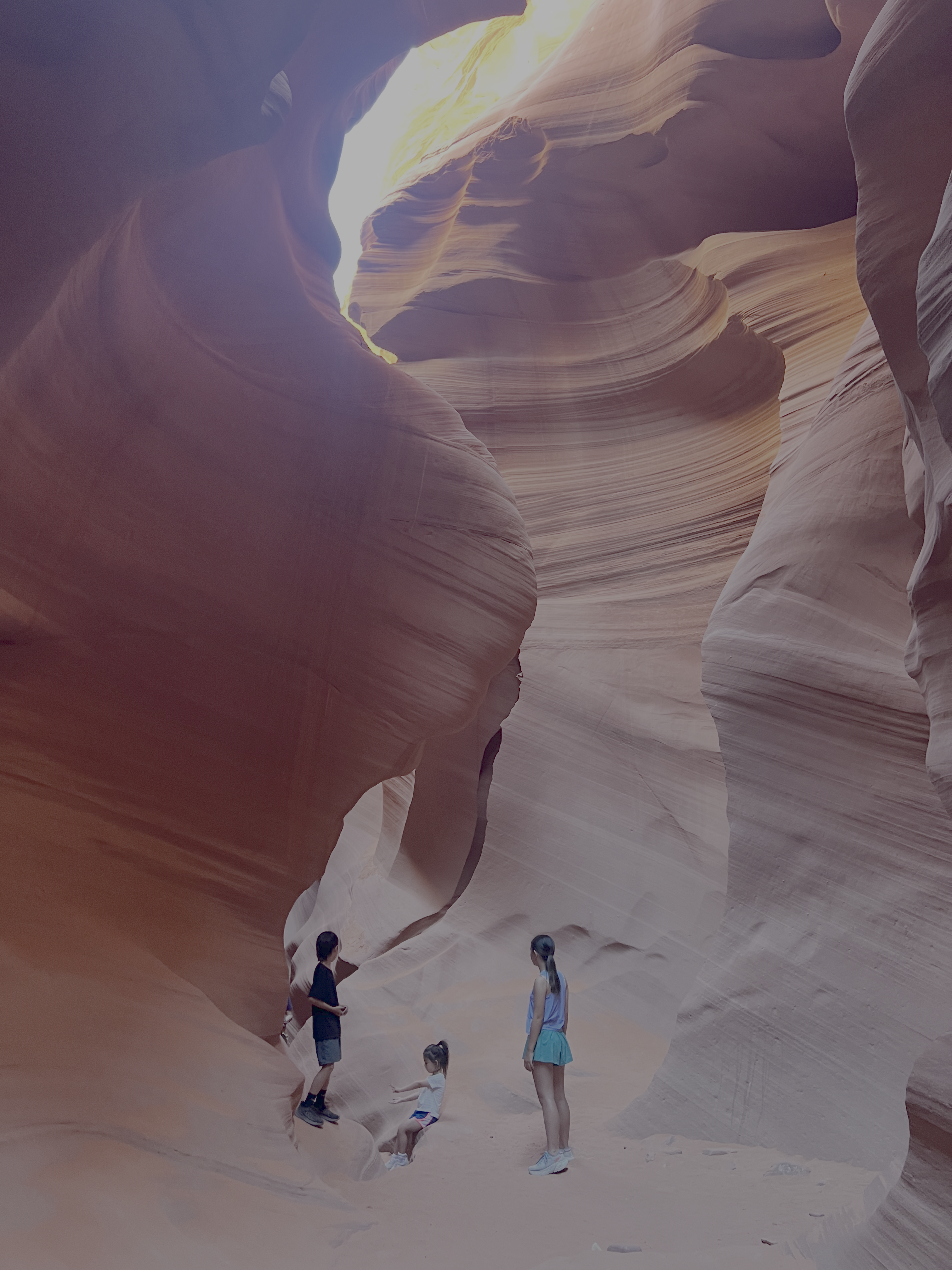 Three people stand in a narrow, winding sandstone canyon with light filtering from above.