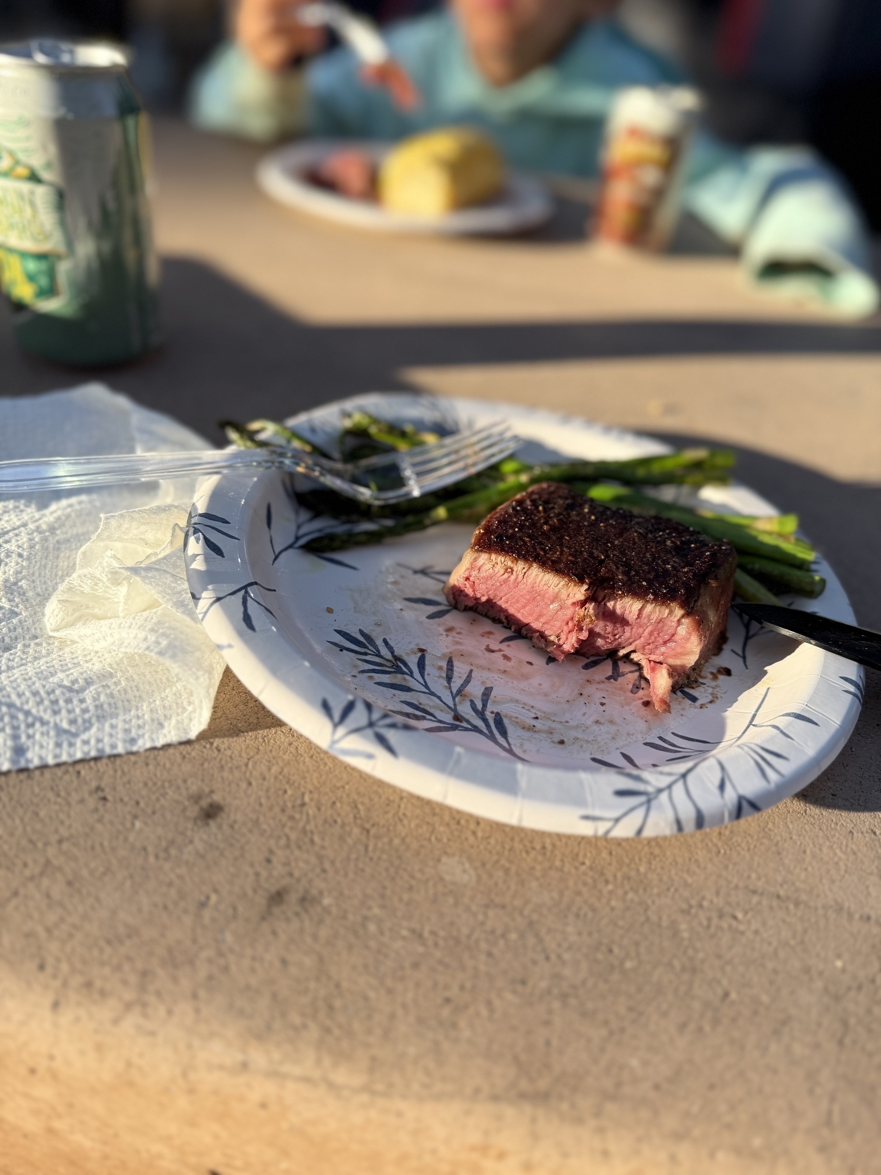 A plate with a partially eaten steak and asparagus is placed on a table next to a can and napkin.